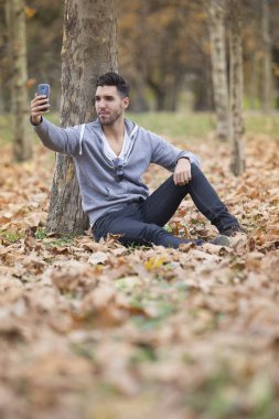Yakışıklı adam doğada onun smartphone ile selfie fotoğraf çekmek. Sonbahar. Kopya alanı