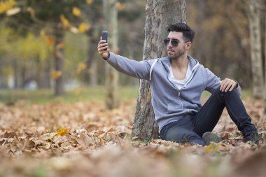 Yakışıklı adam doğada onun smartphone ile selfie fotoğraf çekmek. Sonbahar. Kopya alanı