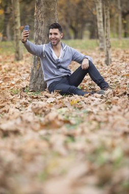 Yakışıklı adam doğada onun smartphone ile selfie fotoğraf çekmek. Sonbahar. Kopya alanı