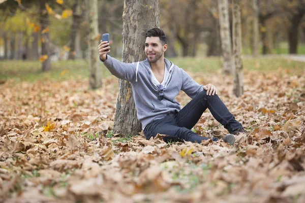 Yakışıklı adam doğada onun smartphone ile selfie fotoğraf çekmek. Sonbahar. Kopya alanı