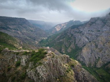 Dağın tepesindeki, yüksek sıradağlarla çevrili küçük şapelin hava aracı görüntüsü, turistler etrafta dolaşıyor.