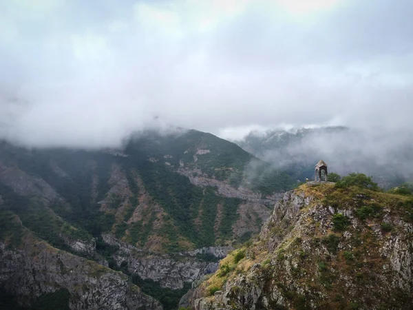 Dağın tepesindeki, yüksek sıradağlarla çevrili küçük şapelin hava aracı görüntüsü, turistler etrafta dolaşıyor.