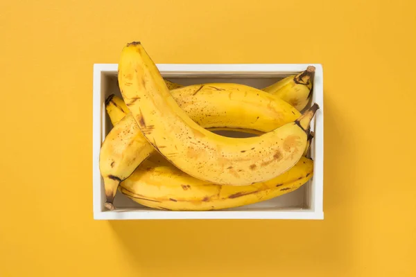 明るい黄色の背景の白いボックスに熟したバナナ 夏のテーマ — ストック写真