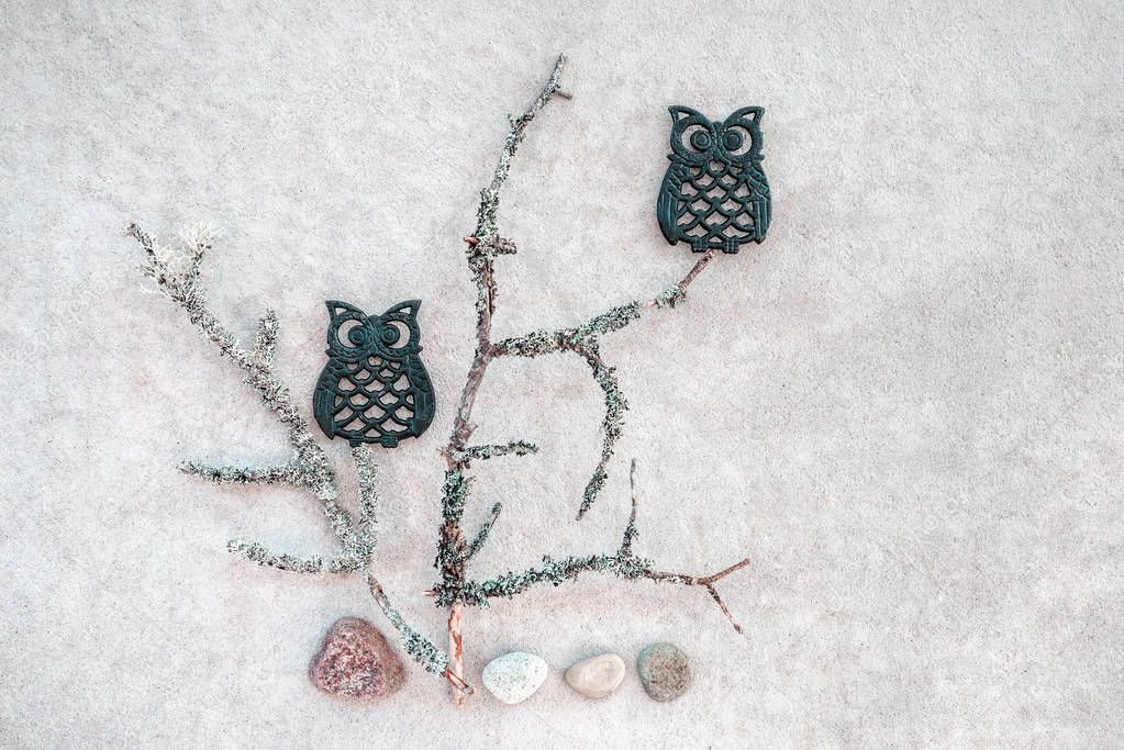Simple and beautiful Nordic nature. Mossy twigs, stones and two iron owls. Flat lay composition on concrete background.