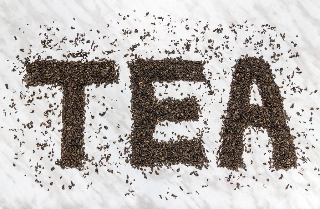 The word TEA written with Gunpowder green tea leaves, on marble background.