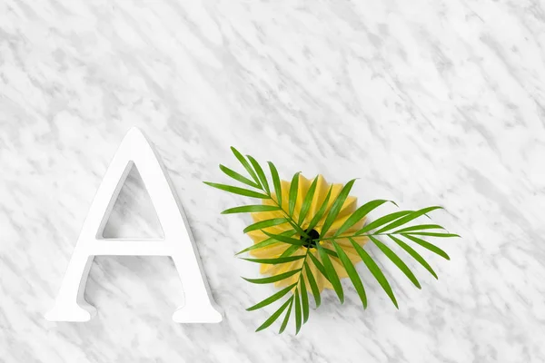 Letter A and green palm leaves in a yellow ceramic vase, on marble background.
