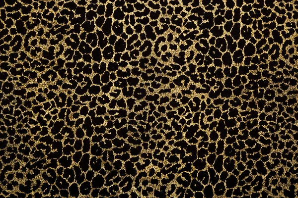 Black fabric with metallic golden leopard fur print. Retro fashion background.