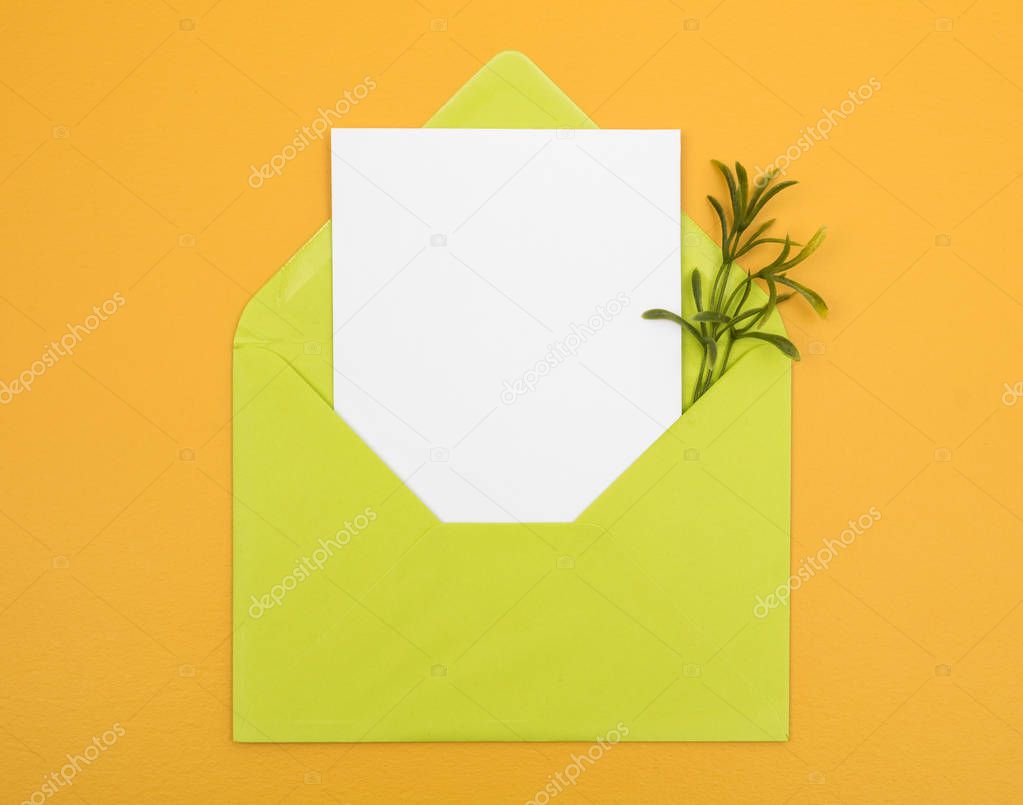 Green envelope with blank white card on bright yellow background. Joyful colors.