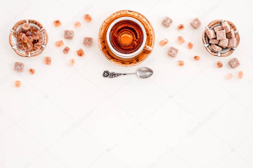 Cup of tea and pieces of brown sugar, on white surface with copy space.