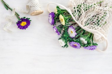Beyaz ahşap arka plan üzerinde bir örgü çanta asters