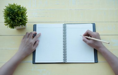 Kadın sarı bir arka plan ile bir kil kitap kitap yazdı. Üstten görünüm.