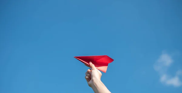 Men's hands hold a red paper rocket with a bright blue background.