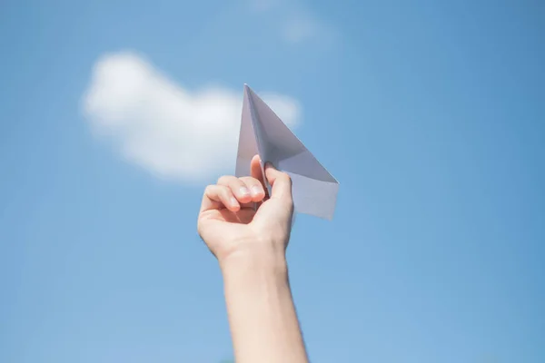 Men\'s hands holding a white paper rocket with a bright blue background.