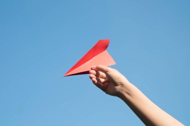 Parlak mavi arka plan ile bir kırmızı kağıt roket tutan kadın el.