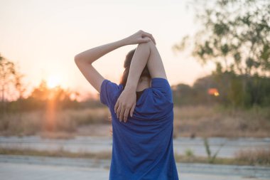 Genç kadın parkta egzersiz öncesine egzersiz. O düşen güneşin arka plan ile fizik muayene için kollarını uzattı.