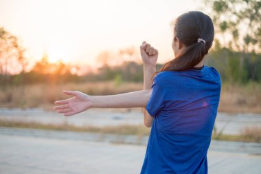 Genç kadın parkta egzersiz öncesine egzersiz. O düşen güneşin arka plan ile fizik muayene için kollarını uzattı.