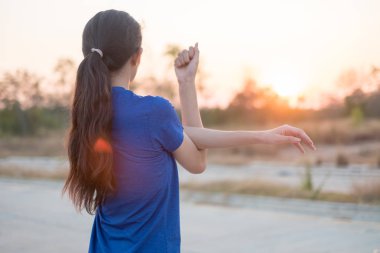 Genç kadın parkta egzersiz öncesine egzersiz. O düşen güneşin arka plan ile fizik muayene için kollarını uzattı.