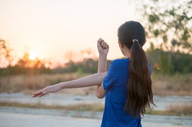 Genç kadın parkta egzersiz öncesine egzersiz. O düşen güneşin arka plan ile fizik muayene için kollarını uzattı.