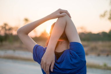 Genç kadın parkta egzersiz öncesine egzersiz. O düşen güneşin arka plan ile fizik muayene için kollarını uzattı.