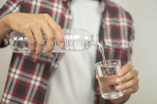 Mann hält eine Flasche Wasser in der Hand und gießt Wasser in ein Glas. Stockbild