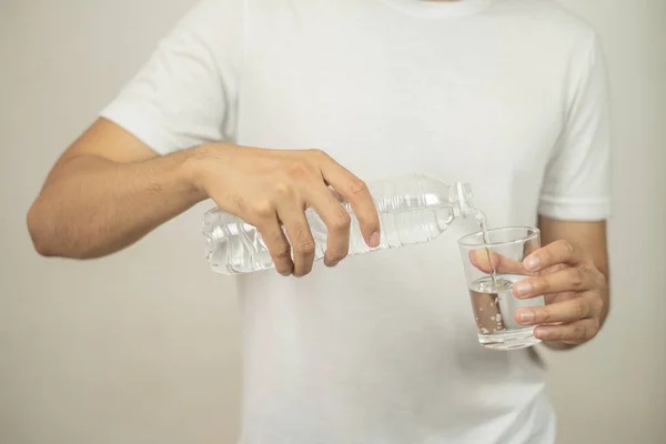 Mann hält eine Flasche Wasser in der Hand und gießt Wasser in ein Glas. lizenzfreie Stockbilder