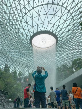 Singapur, Singapur - 1 Mayıs 2019: Kimliği belirsiz kişiler Singapur Changi Uluslararası Havaalanı'ndaki Yağmur Girdab Şelalesi önünde fotoğraf çekiyor.