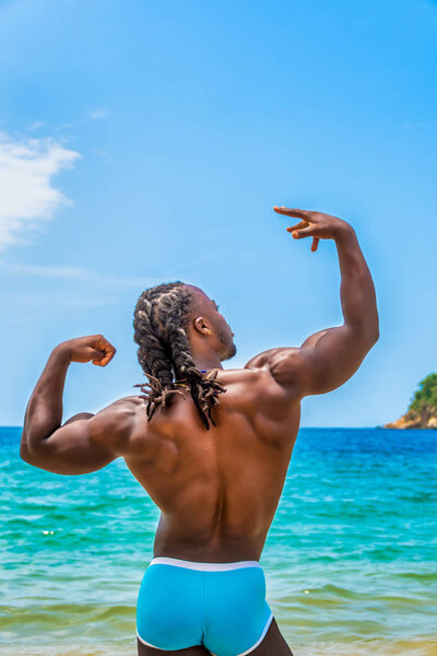 Молодой, красивый, мускулистый, без рубашки афроамериканец, позирует в воде, показывая свою спину, на пляже Елапа близ Пуэрто-Вальярта, Мексика
.