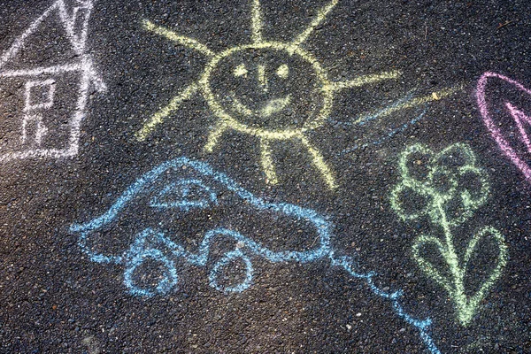 Chalk drawing on a asphalt pavement, sun, car, flower, house.