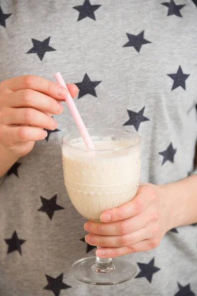 Young woman with a big glass of healthy smoothie served with a straw and oats. Hands holding milkshake. Stars background. Dairy snack or breakfast.