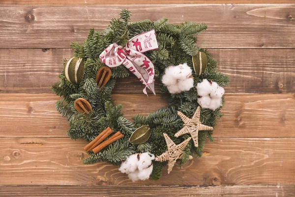 Closeup of Christmas wreath with cinnamon, cotton ears and ribbon decorations on wooden background. Winter, xmas and season greeting.