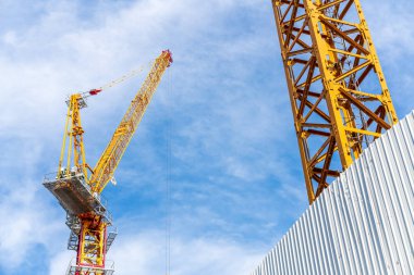 Arka planda bulut ve mavi gökyüzü ile inşaat alanında çalışan vinç.