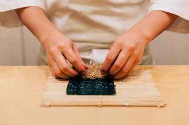 Japon Omakase Chef el ahşap mutfak tezgahında elini tarafından düzgünce bir tuna Nori Handroll haddeleme.