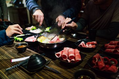 Erkekler ve kadınlar elleri buhar ile çubukları tarafından sıcak tencere shabu açık çorba tabanında orta nadir dilim Wagyu A5 sığır eti ve Kurobuta domuz pinching.