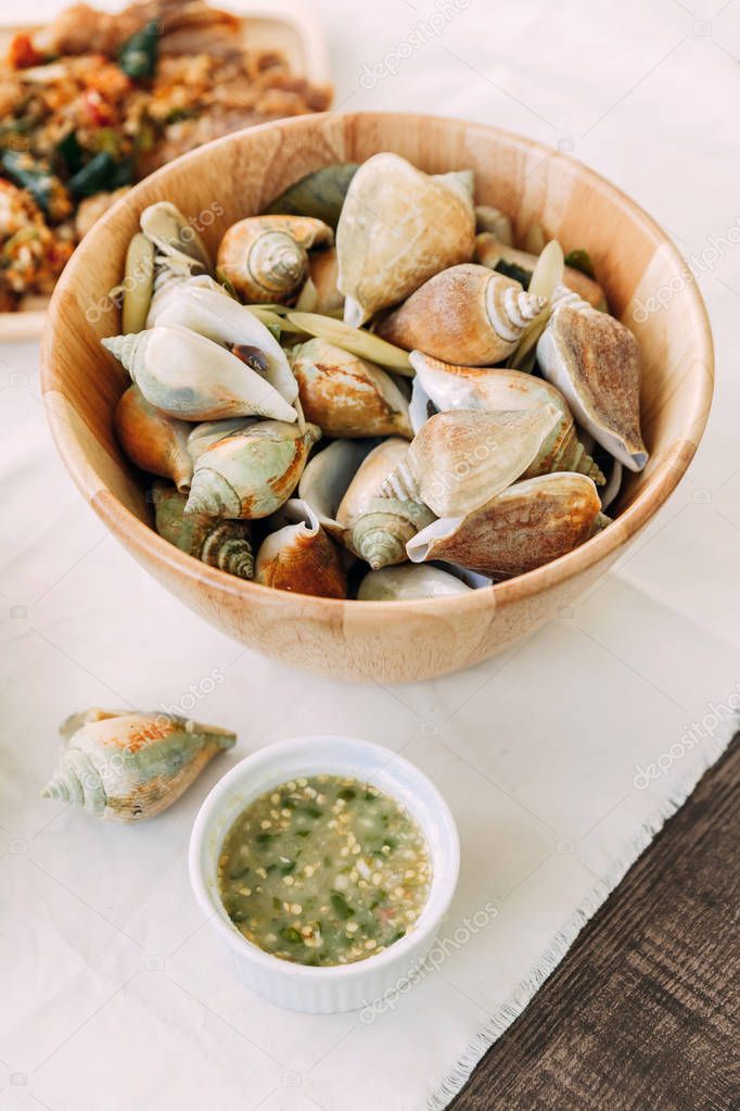 Grilled Laevistrombus Canarium in shells in wooden bowl served with Thai spicy seafood sauce.