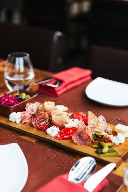 Prosciutto, pastırma, salam ve sosis ile ahşap tahta üzerinde soğuk kesim. Kıymalı yemek masasında turşu ve zeytin ile servis edilen et tabağı mezeleri.