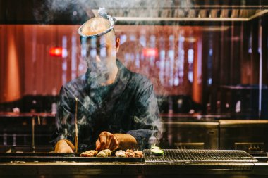 Japon Yakitori Chef zencefil, sarımsak ve soya sosu ile marine tavuk ızgara duman bir sürü.