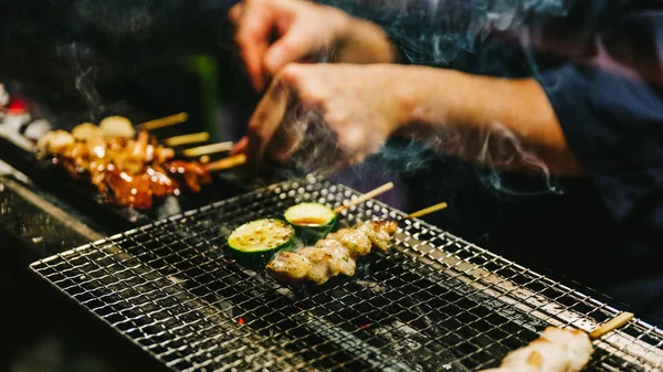 Japon Yakitori Chef ızgara tavuk zencefil, sarımsak ve soya sosu ve salatalık duman bir sürü ile marine yakın çekim eller.