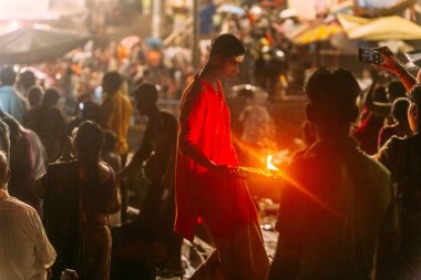 Papa LıkAth Tapınağı yakınlarındaki Kutsal Dasaswamedh Ghat'ta Varanasi Ganga Aarti'de insanları kutsaması için kırmızı bezle yürüyen kırmızı bez giyen çocuk.