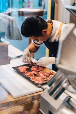 Asian butcher is arranging premium rare slices many parts of Wagyu A5 beef with high-marbled texture on stone plate in kitchen. Served for Yakiniku (Grilled Meat). clipart