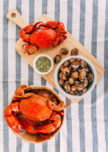 Top view of Steamed Giant Mud Crabs in wooden bowl served with Thai spicy seafood sauce and Grilled Laevistrombus Canarium in shell.