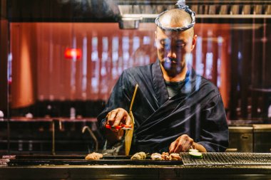 Japon Yakitori Chef zencefil, sarımsak ve soya sosu ile marine tavuk ızgara duman bir sürü.