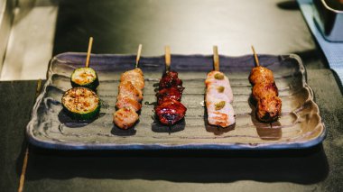 Yakitori (Japon Usulü Izgara Tavuk Şişler) tavuk, iç organ ve salatalık siyah taş plaka üzerinde servis.