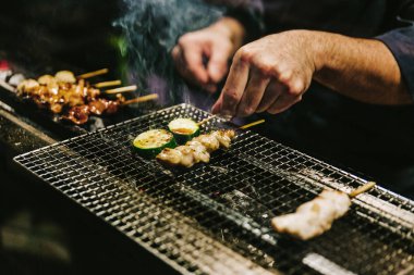Japon Yakitori Chef ızgara tavuk zencefil, sarımsak ve soya sosu ve salatalık duman bir sürü ile marine yakın çekim eller.