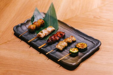Yakitori (Japon Usulü Izgara Tavuk Şişler) tavuk, iç organ ve salatalık siyah taş plaka üzerinde servis.