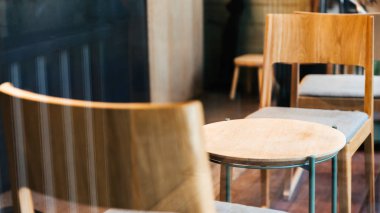 Kafe içinde yakın çekim ahşap sandalyeler ve boş alçak masa. Sıcak ve rahat bir atmosfer.