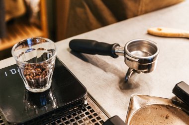Kahve tezgahında boş kahve öğütücü grup kolu ile ağırlık ölçeğinde shot cam içinde Kahve çekirdekleri.