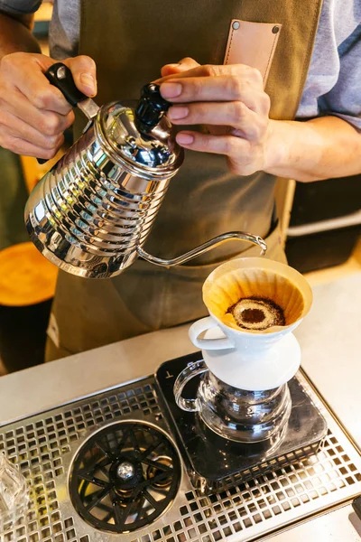 Barista making pour-over coffee with alternative method called Dripping. Coffee grinder, coffee stand and pour-over on a wooden table.