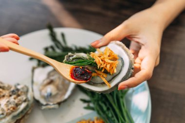 Kızarmış soğan, Chili Paste, Acacia pennata ve Tay tarzı deniz ürünleri sosu ile Tepesi elinde kabuk taze Oyster.