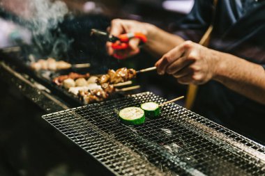 Japon Yakitori Chef ızgara tavuk zencefil, sarımsak ve soya sosu ve salatalık duman bir sürü ile marine yakın çekim eller.