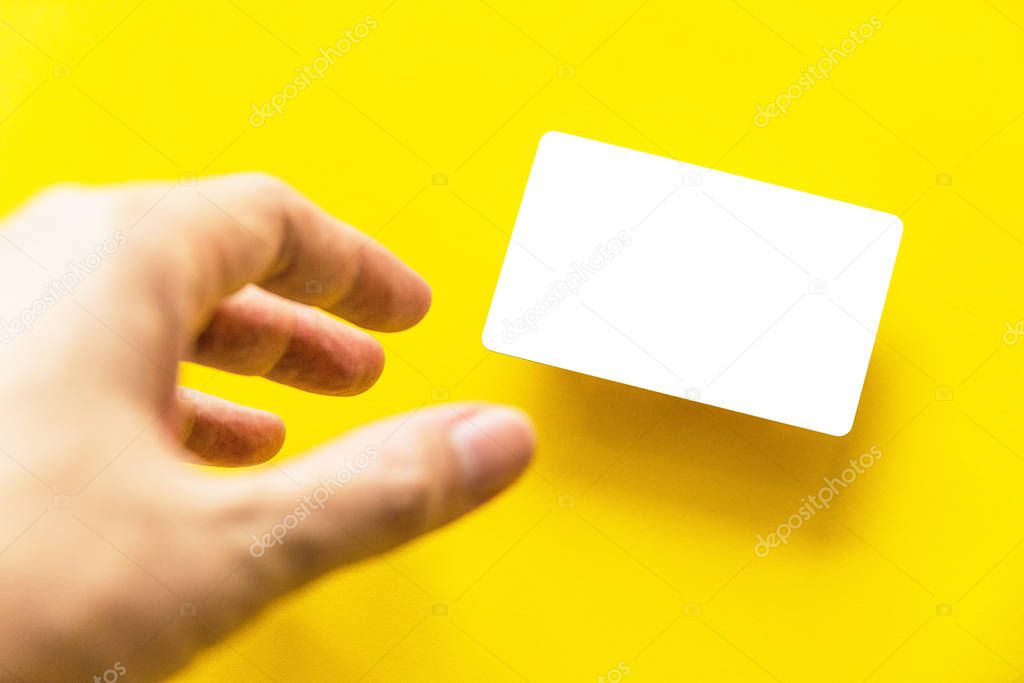 Foreground hand reaching empty white business card with shadow on yellow paper background.